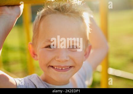 Allegri giorni di infanzia. Ritratto di un ragazzino sorridente che gioca su una palestra nella giungla nel parco. Foto Stock