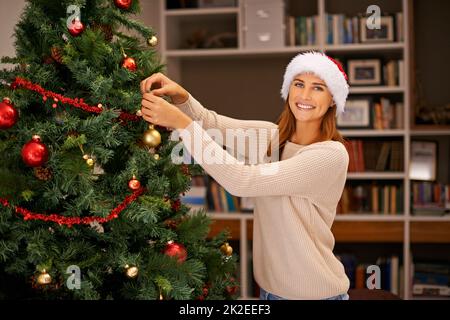 Preparatevi prima che tutti arrivino qui. Scatto di una bella giovane donna che decorare il suo albero di Natale a casa. Foto Stock