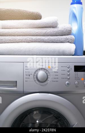 Funzionalità impeccabile per le tue esigenze di lavanderia. Shot di una lavatrice con asciugamani piegati e detersivo sopra di esso. Foto Stock