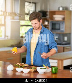 Qual è stato il prossimo passo di nuovo.... Shot di un giovane confuso che guarda gli ingredienti della ricetta su un banco da cucina a casa. Foto Stock