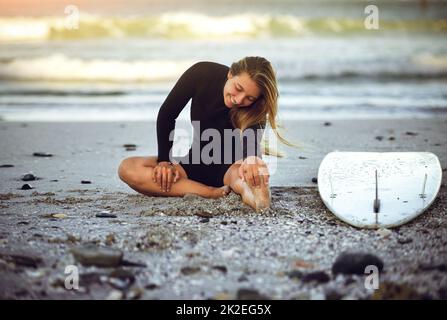 Youve gotta stretching. Scatto a tutta lunghezza di una giovane ragazza attraente surfista che si scalda sulla spiaggia. Foto Stock