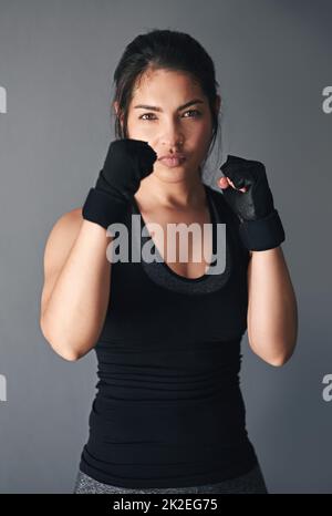 Pronti per una lotta. Studio girato di un kickboxer femminile su sfondo grigio. Foto Stock