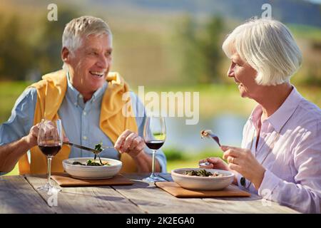 Ancora datando nei loro anni anziani. Scatto corto di una coppia anziana che beve vino mentre si gusta un pasto all'aperto. Foto Stock