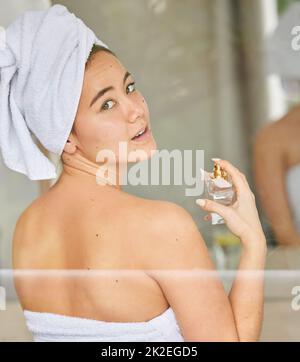 La cura di sé mi fa sentire stupefacente. Shot di una giovane donna spruzzando profumo durante la sua routine di bellezza mattina. Foto Stock