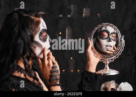 Halloween trucco sul punto. Scatto corto di una giovane donna attraente vestito con il suo costume messicano di Halloween guardando in uno specchio. Foto Stock