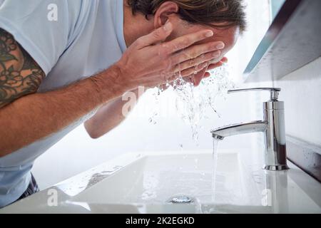 Aiutando la mia pelle a ripristinare il suo equilibrio di pH. Colpo di un uomo che lava il viso nel lavandino del bagno. Foto Stock