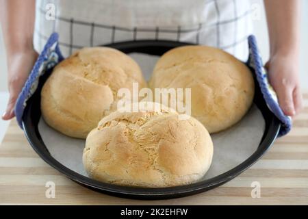 Donna che mostra tre pagnotte fatte in casa di pane in una teglia appena sfornata Foto Stock