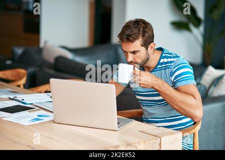 Forse un certo caffè aiuterà. Scatto corto di un bel giovane imprenditore maschio che beve caffè mentre lavora dal suo ufficio domestico. Foto Stock