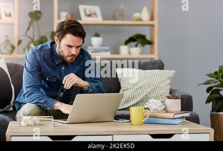 Mette a fuoco in tutto che faccia. Scatto corto di un bel giovane uomo che usa un computer portatile nel suo soggiorno a casa. Foto Stock