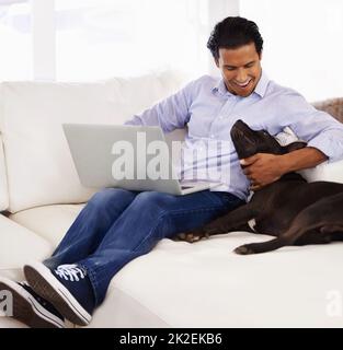 HES sempre al mio fianco. Un bel giovane uomo che accarezza il suo cane mentre lavora su un computer portatile a casa. Foto Stock