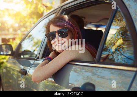 Fare una piccola pausa. Scatto di una giovane donna che fa una pausa e guarda la telecamera mentre si siede sul sedile posteriore di un'auto. Foto Stock