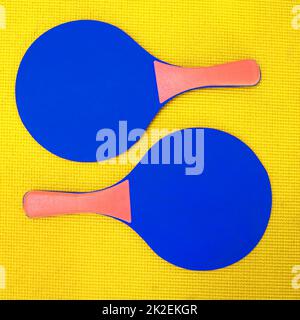 Ci vogliono due volte per il tango. Scatto ad angolo alto di due racchette da ping-pong blu poste su uno sfondo giallo all'interno di uno studio. Foto Stock