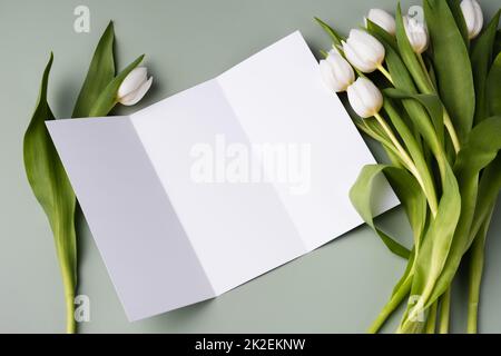 Mockup opuscolo cartaceo su sfondo verde chiaro con un bouquet di belle tulipani bianchi. Foto Stock