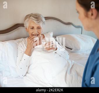 Vitamine per quella spinta di vitalità. Shot di un'infermiera che dà a una donna anziana il suo farmaco per prendere con un bicchiere d'acqua a letto. Foto Stock