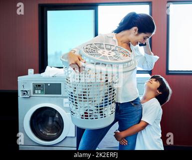 Lascia prima finire la lavanderia poi possiamo giocare. Scatto corto di una giovane madre attraente che fa il bucato con suo figlio a casa. Foto Stock