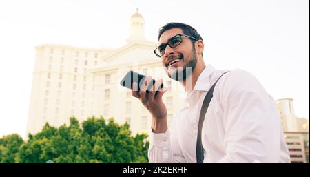 Bene thats un senso di illuminare sul mio giorno. Scatto di un bel giovane uomo d'affari utilizzando il suo cellulare per fare una nota vocale mentre si cammina per la città. Foto Stock