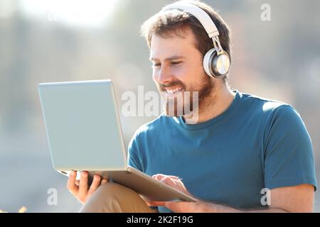 Uomo felice che indossa le cuffie con il computer portatile Foto Stock