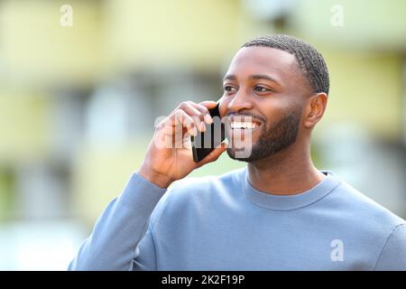 Uomo felice con pelle nera parla al telefono all'esterno Foto Stock