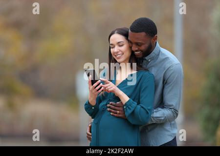 Moglie incinta e suo marito che controlla lo smartphone Foto Stock