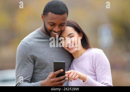 Felice coppia interracial che controlla lo smartphone all'aperto Foto Stock