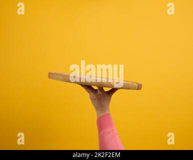 donna che tiene in mano un piano di pizza vuoto rotondo di legno, parte del corpo su sfondo giallo Foto Stock