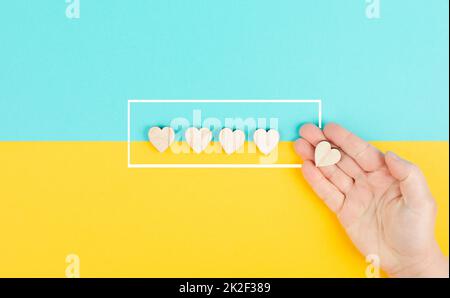 Cinque cuori su uno sfondo blu e giallo, mano mettere l'ultimo cuore in fila, valutare, dare feedback, valutazione aziendale Foto Stock