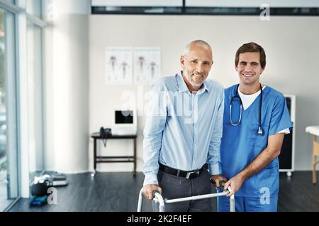 Tornando sulla strada della ripresa. Ritratto di un infermiere di sesso maschile che assiste un paziente anziano con un camminatore. Foto Stock