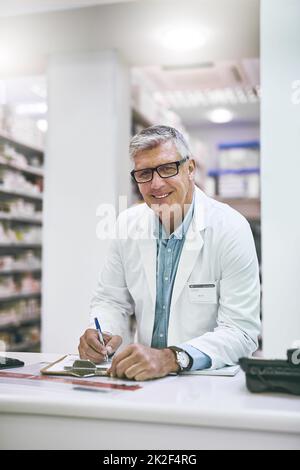 Ho tutto il necessario qui. Ritratto di un farmacista maschio maturo sicuro facendo note in un libro sul banco mentre si guarda la fotocamera. Foto Stock