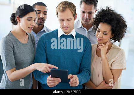 Ogni opinione conta. Un gruppo di colleghi diversi che utilizzano un tablet digitale mentre si trovano in ufficio. Foto Stock