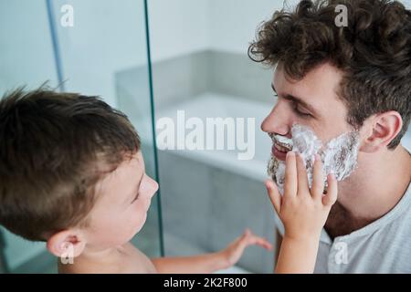 Lascilo fare esso per voi papà. Shot di un bambino strofinando crema di rasatura sul viso dei padri nel bagno di casa. Foto Stock