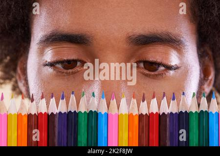 HMM, tanti colori.... Vista ritagliata di un uomo africano che guarda da vicino una fila di colorati pastelli a matita. Foto Stock