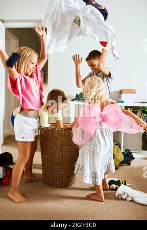 I suoi vestiti pioventi. Shot di piccoli fratelli gettando la lavanderia in aria a casa. Foto Stock