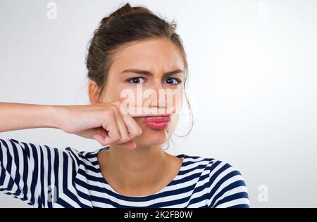 Non mi troverò mai con questo travestimento. Ritratto di una bella giovane donna usando il dito per fare un baffi. Foto Stock