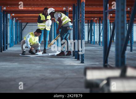 Parliamo perfettamente di ingegnere. Immagine di un gruppo di appaltatori che utilizza un piano per pianificare in magazzino. Foto Stock