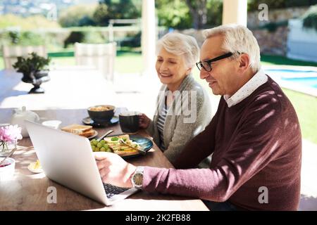 Connessione con il resto del mondo. Scatto di una coppia anziana affettuosa utilizzando un computer portatile mentre si gusta un pasto insieme all'aperto. Foto Stock