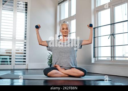 Non avete bisogno dei pesi grandi per ottenere un workout adeguato. Ritratto di una donna matura allegra che pratica yoga mentre fa uso di pesi all'interno di uno studio durante il giorno. Foto Stock