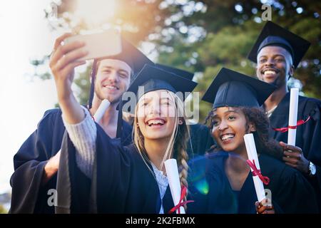 Questo è un giorno che non dimentichi mai. Scatto corto di un gruppo di studenti universitari che prendono un selfie il giorno della laurea. Foto Stock