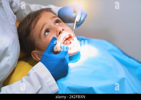 Basta cercare di tenere fermo il mio caro. Scatto di un ragazzino che si trova su una sedia dentista mentre si ottiene un controllo dal dentista. Foto Stock