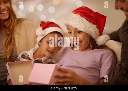 Proprio quello che volevo. Una bambina che disavvolge un regalo di Natale mentre è circondata dalla sua famiglia. Foto Stock