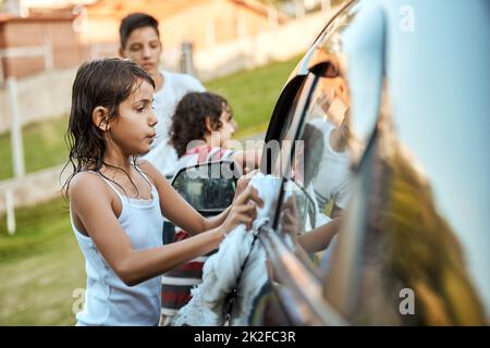 Alcuni scrubbing qui e alcuni scrubbing là. Shot di un gruppo di bambini allegri che lavano i loro genitori auto insieme fuori durante il giorno. Foto Stock