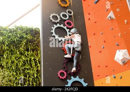 Bambini arrampicata sulla parete nel centro divertimenti. Corsi di arrampicata per bambini. Bambina in vestito arrampicata attrezzatura arrampicata salire in alto. Divertimento estremamente attivo per i bambini. Bambina caucasica di 5 anni. Foto Stock