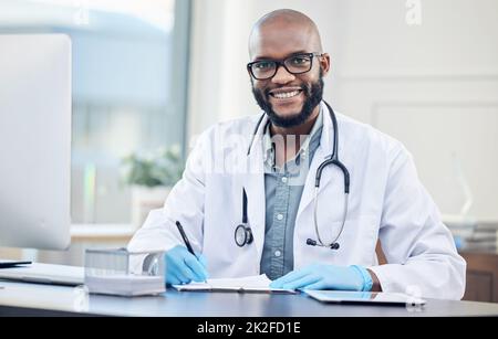 Come posso farti sentire meglio. Scatto di un bel medico giovane seduto da solo nella sua clinica e prendere appunti. Foto Stock