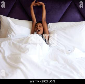 Ben riposato. Scatto corto di una giovane donna attraente yawning e stretching mentre si sveglia in su a letto. Foto Stock