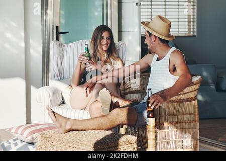 Godendo una giornata molto necessaria di riposo. Shot completo di una giovane coppia affettuosa che beve birre mentre si rilassa sul patio. Foto Stock