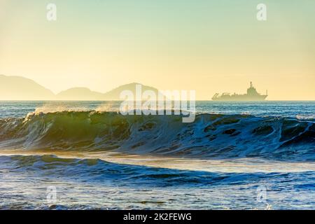 Onde che si rompono sulla spiaggia durante l'alba con la nave che attraversa l'orizzonte Foto Stock