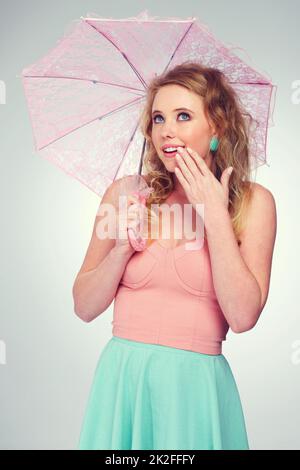 Oops, quella macchina del tempo ha funzionato realmente. Studio shot di una bella ragazza bionda in possesso di un parasolo guardando sorpreso. Foto Stock