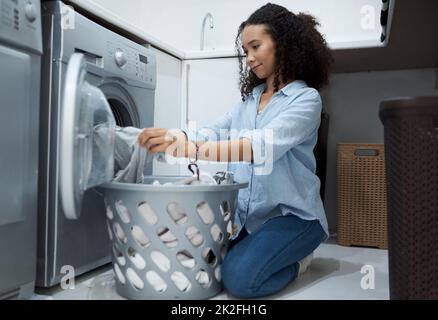 La mia casa puzza come una lavanderia automatica. Shot di una giovane donna che si prepara a lavare un carico di lavanderia a casa. Foto Stock