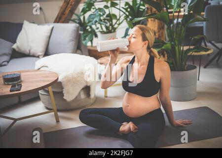 Giovane felice e allegro bella donna incinta prendere una pausa, idratante, bere acqua dalla botola dopo casa benessere programma di allenamento. Foto Stock