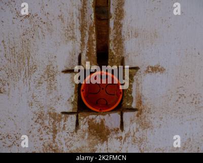 Scatola posteriore rotonda in plastica arancione per connettore femmina o interruttore inserita nel foro praticato sulla parete. Nuova installazione elettrica, foro presa sulla parete in argilla, r Foto Stock