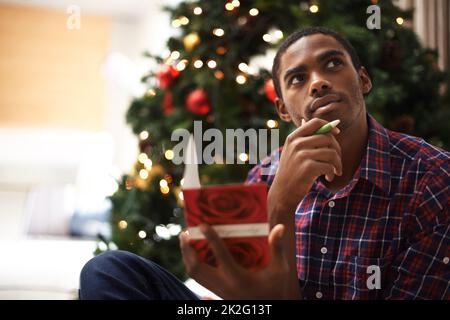 Natale è il mio periodo preferito dell'anno. Un bel giovane che pensa a qualcosa da scrivere in un biglietto di natale. Foto Stock